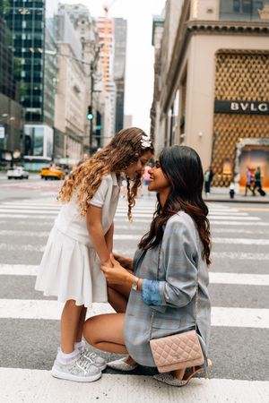 Two friends sitting on a city street in front of luxury retail stores, sharing a playful moment together.