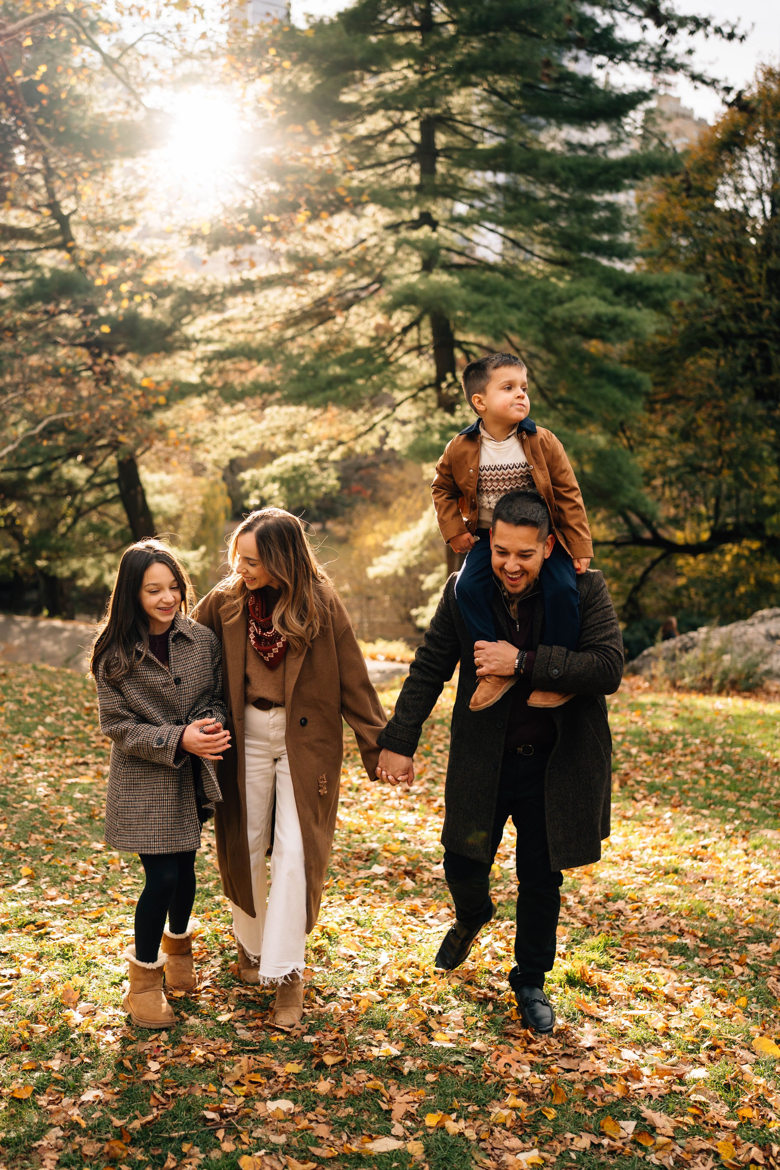 Three people enjoying a playful autumn moment in a sunlit forest with fallen leaves on the ground.