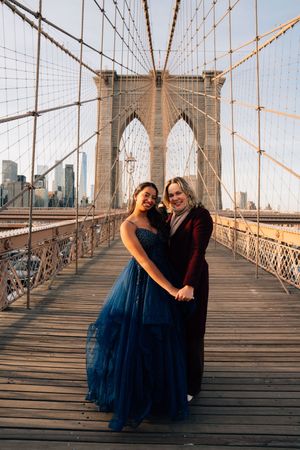 A couple embraces during a romantic sunset photoshoot on the iconic Brooklyn Bridge's wooden walkway.