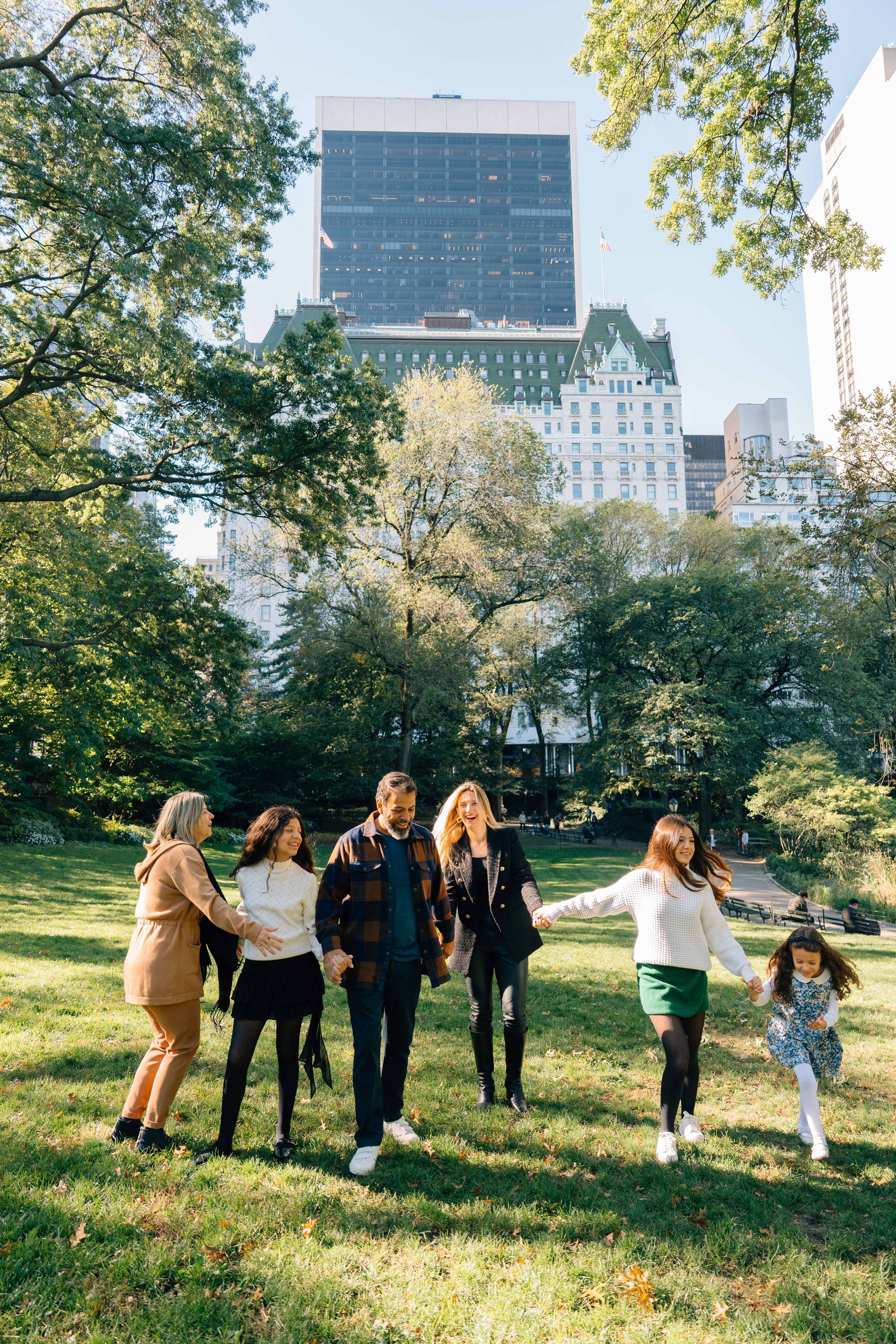 A group enjoying a sunny autumn day in Central Park with NYC skyscrapers and fall foliage in the background.