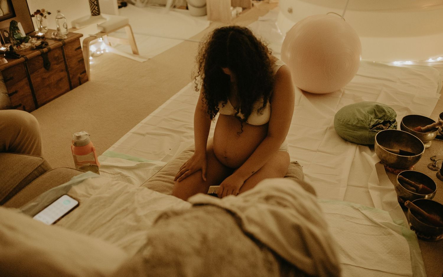 Woman practicing meditation on a massage table surrounded by singing bowls and soft ambient lighting.