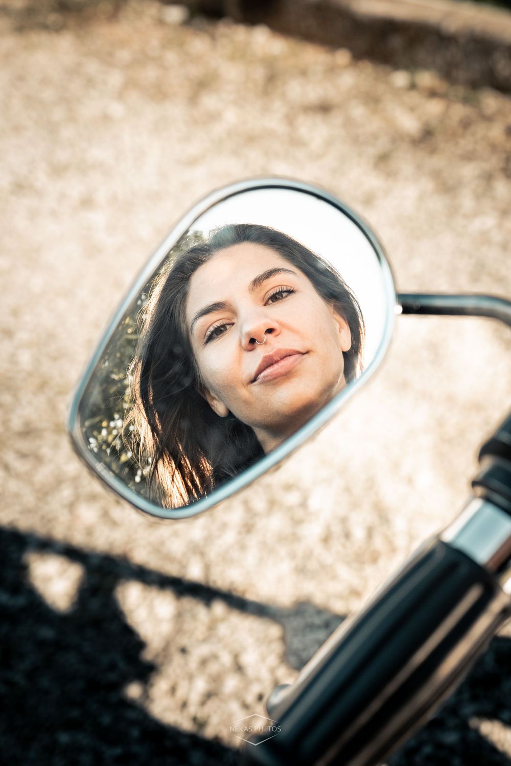Woman's face reflected in a motorcycle side mirror outdoors on a sunny day.