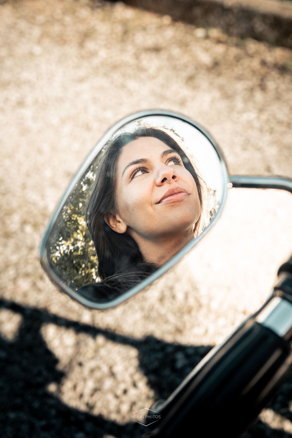 Woman's face reflected in a motorcycle side mirror, gazing upward with a serene expression outdoors.