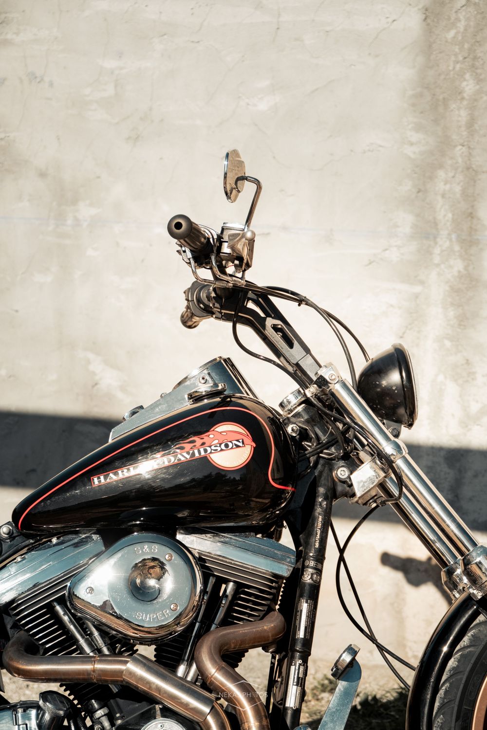 A classic black Harley-Davidson motorcycle with chrome details parked against a concrete wall.