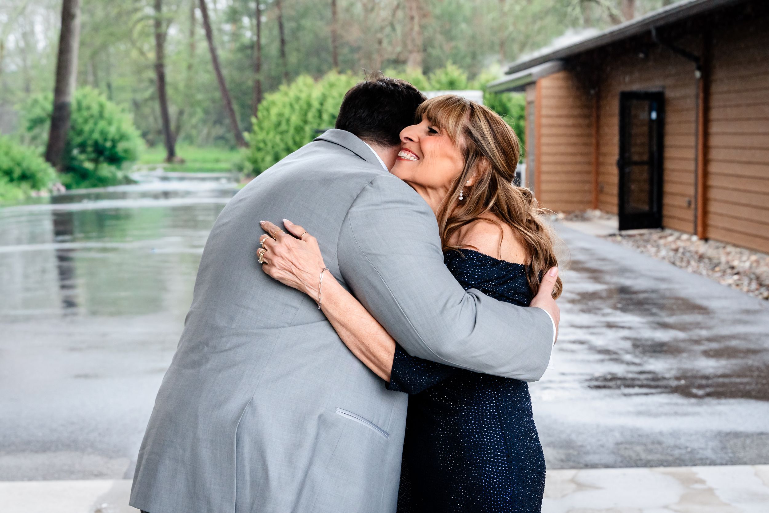 Couple sharing warm embrace outside rustic lodge venue on rainy wedding day.
