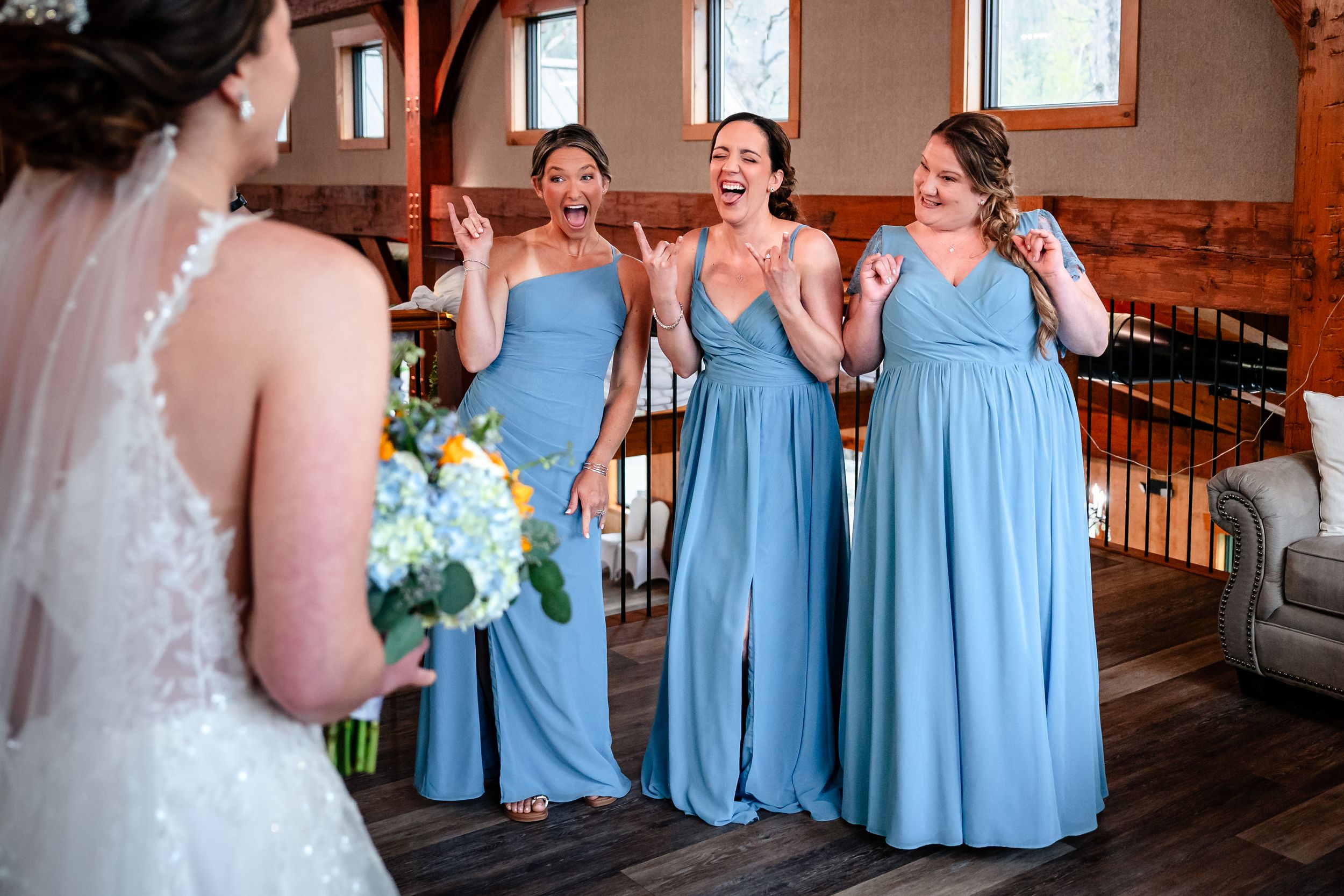 Bridesmaids in blue dresses react with excitement during the bride's first look reveal.
