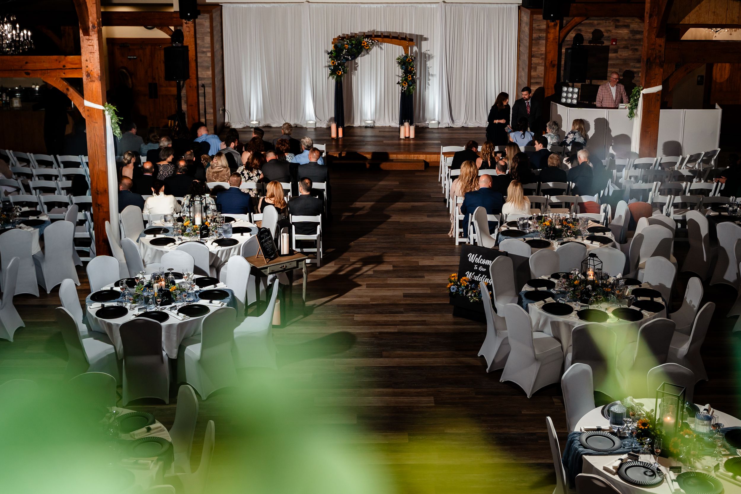 Elegant wedding reception setup in rustic barn with round tables and floral arch altar.