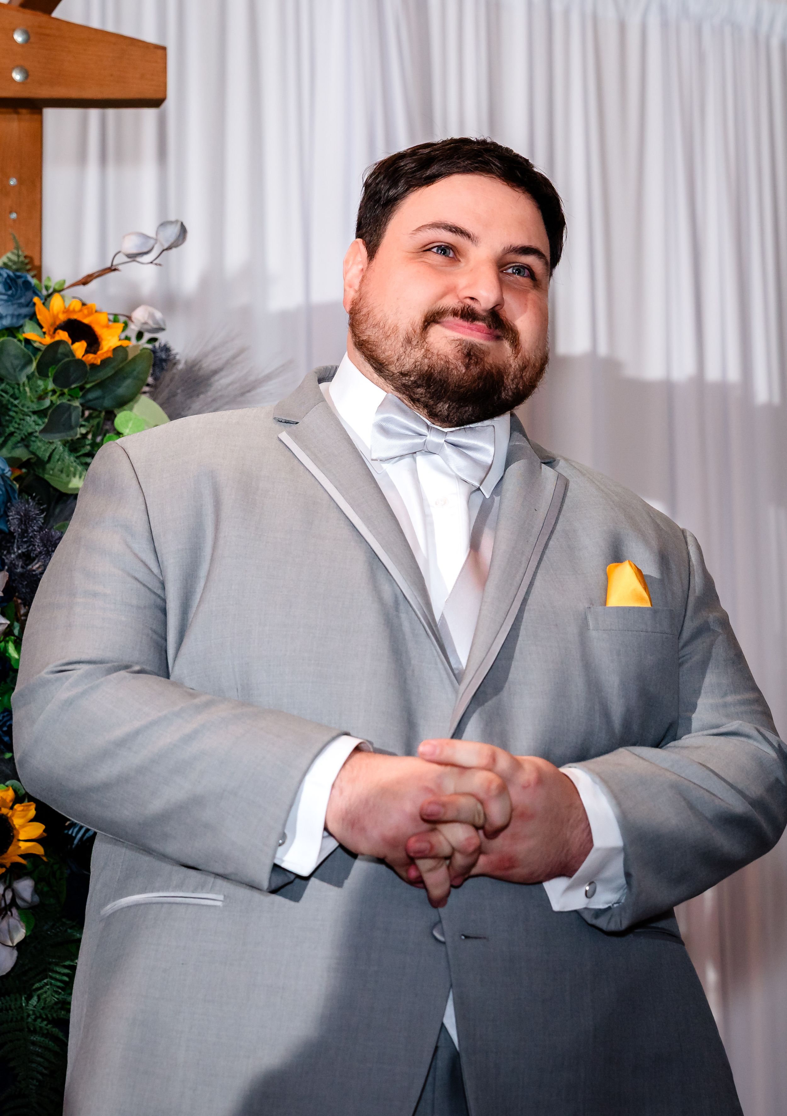Groom in gray tuxedo with yellow pocket square smiling at wedding ceremony altar.