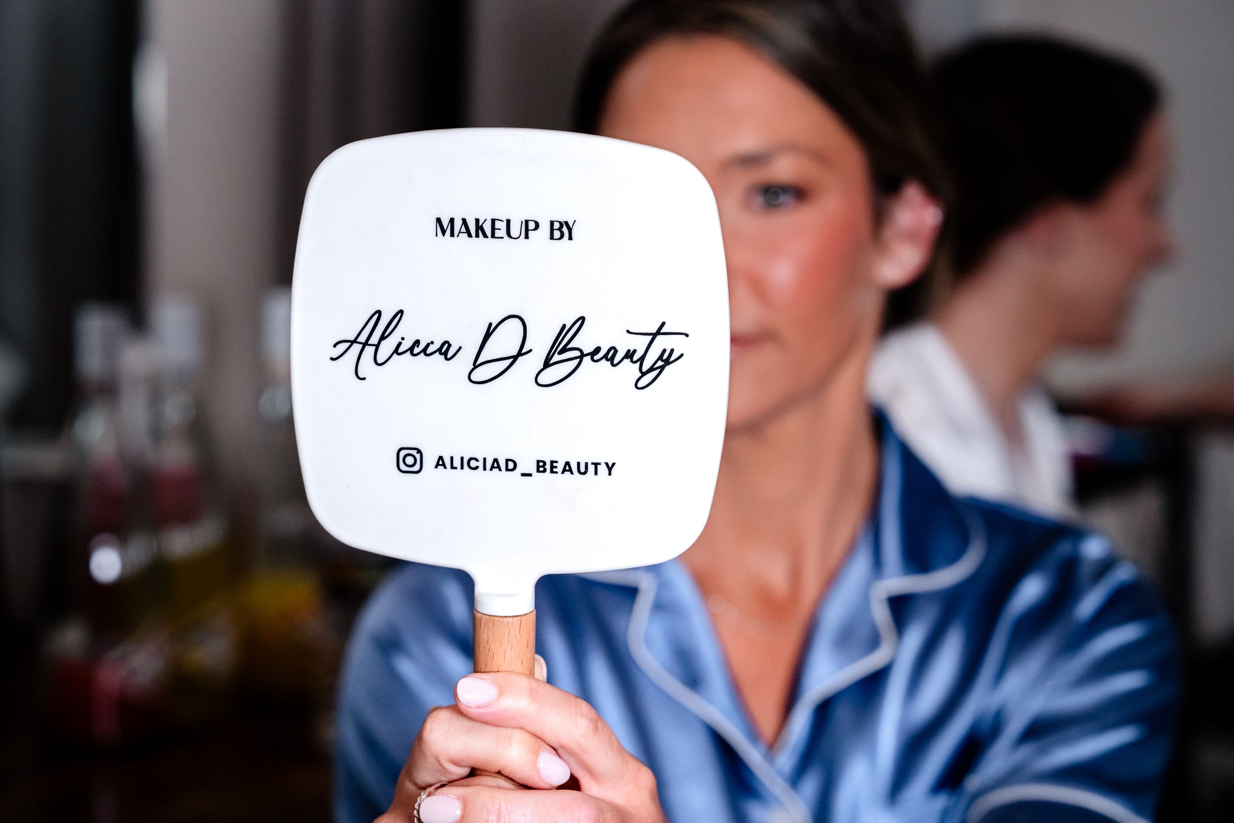 Makeup artist holds a branded Alicia D Beauty mirror at a bridal preparation session.