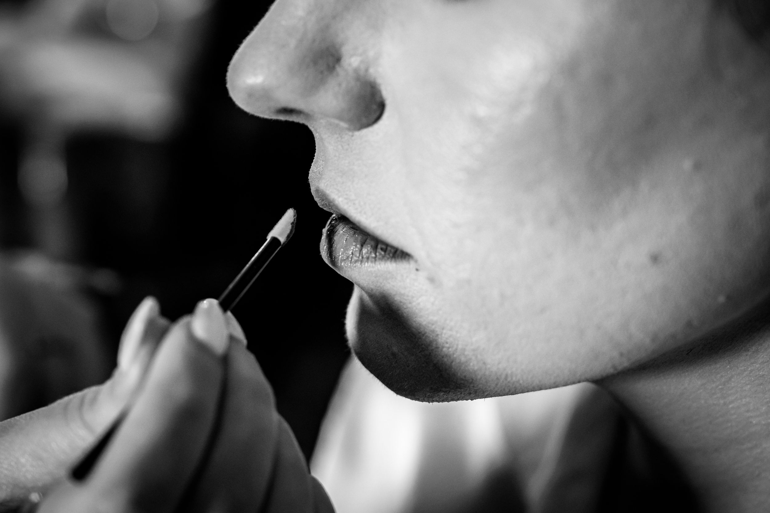 Close-up black and white photo of makeup artist applying lipstick with a brush.