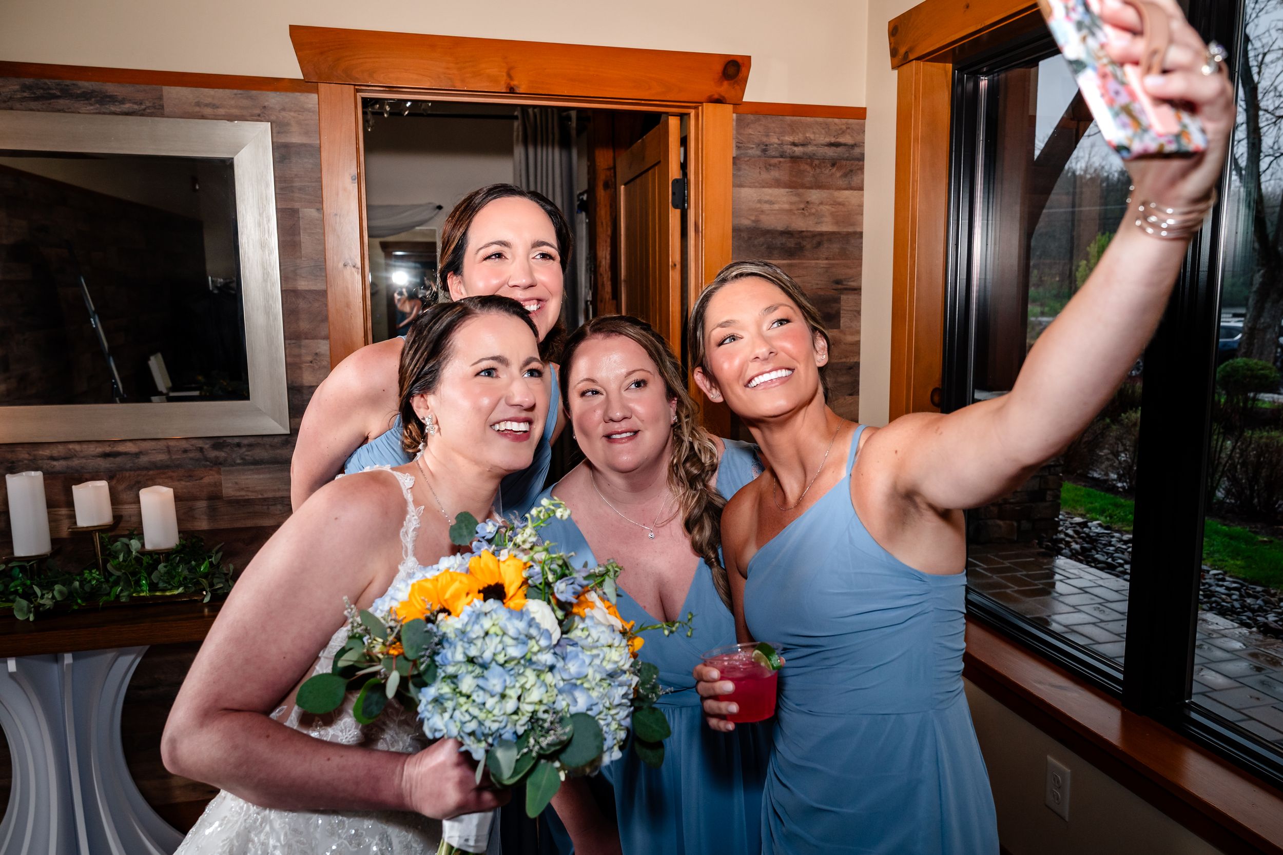 Bride and bridesmaids in blue dresses take a fun selfie at wedding reception.