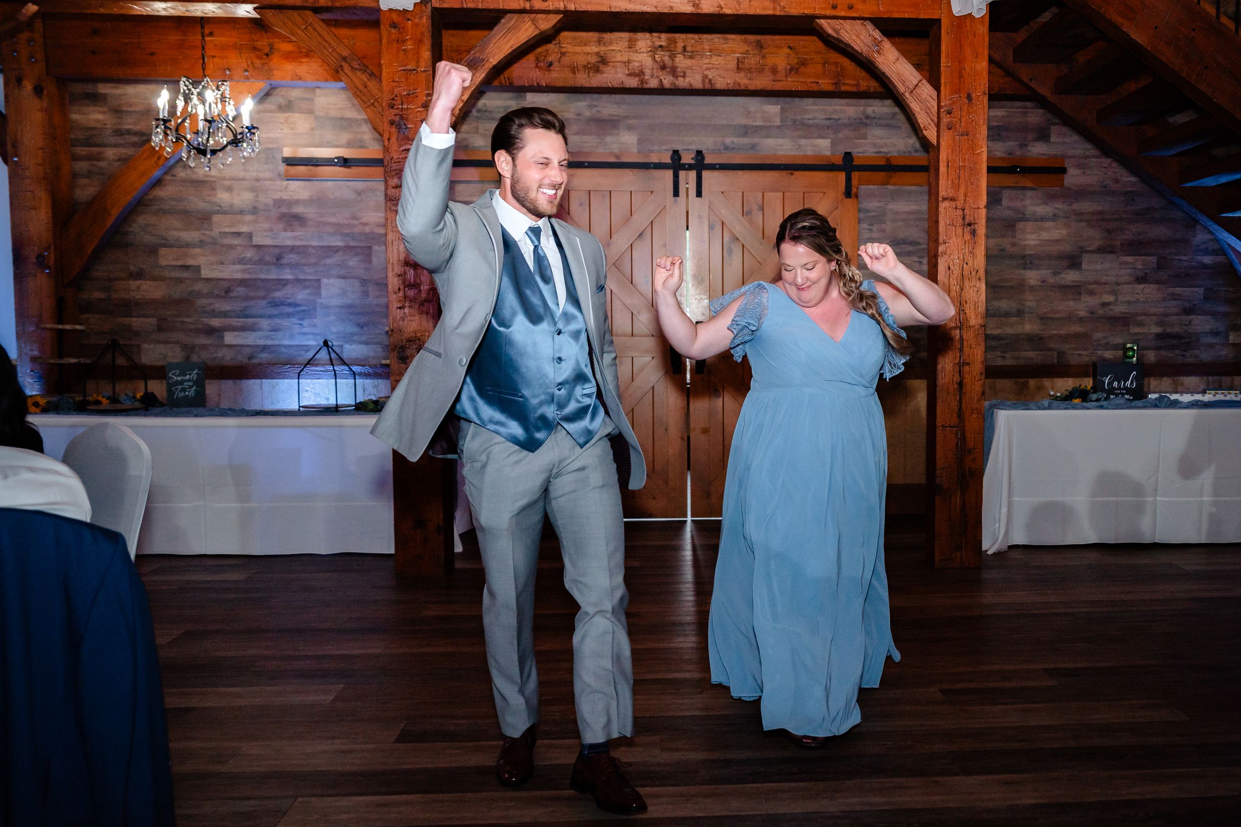 Groom and guest making a fun entrance onto the dance floor at a rustic barn wedding reception.