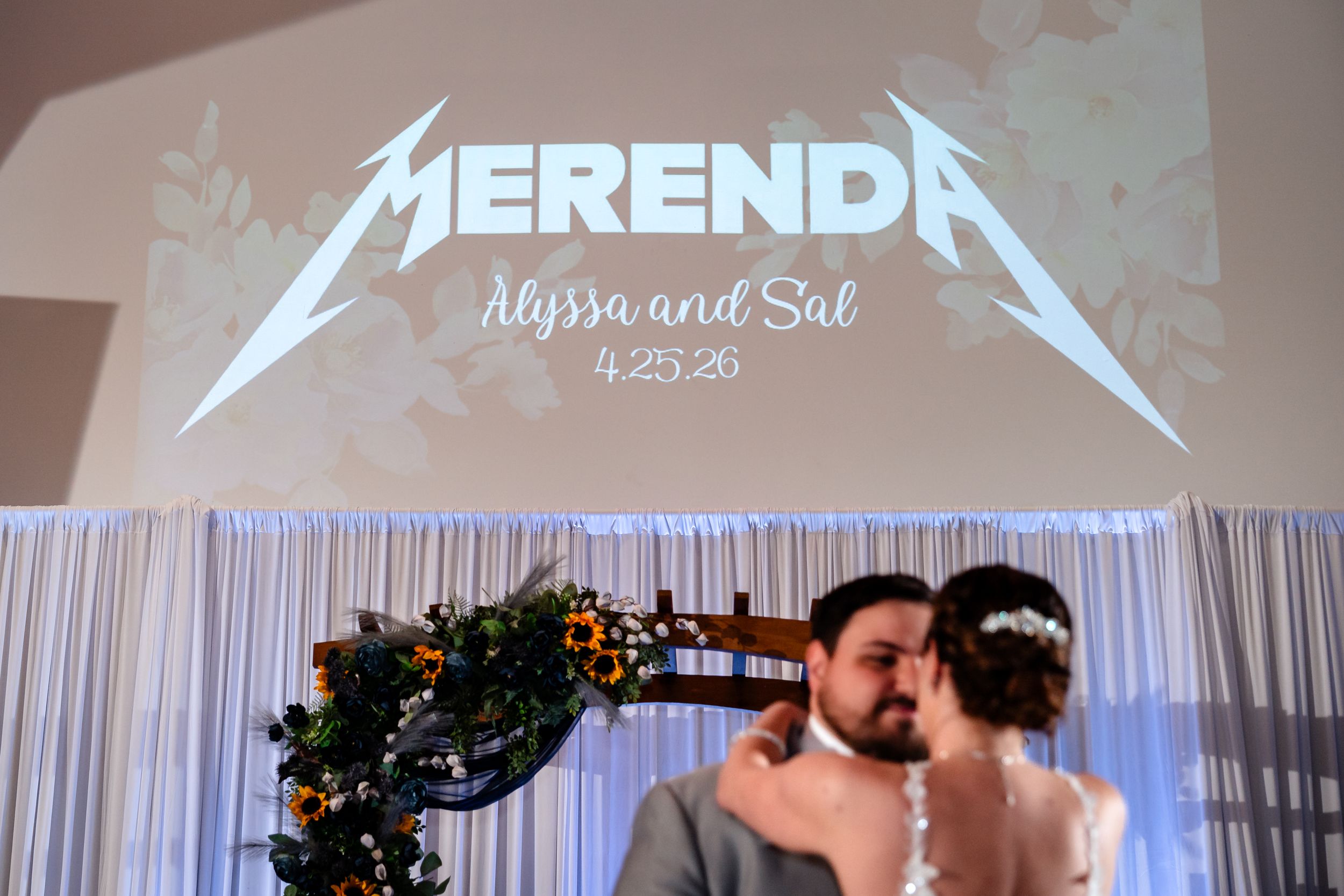 Newlyweds kiss beneath a Metallica-style wedding logo reading Merenda, Alyssa and Sal, 4.25.26.