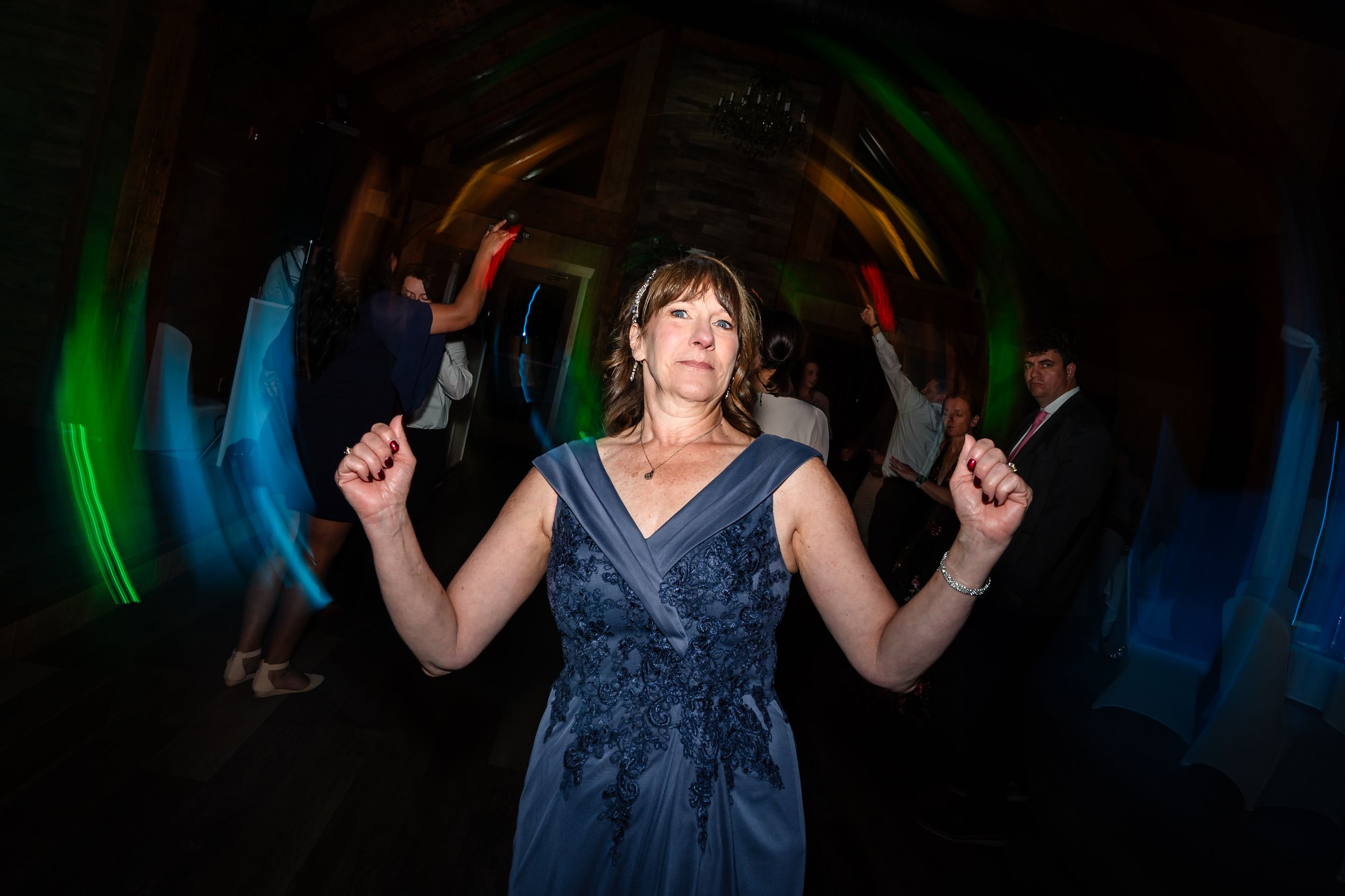 Woman in blue gown dancing joyfully at a wedding reception with colorful lights in the background.