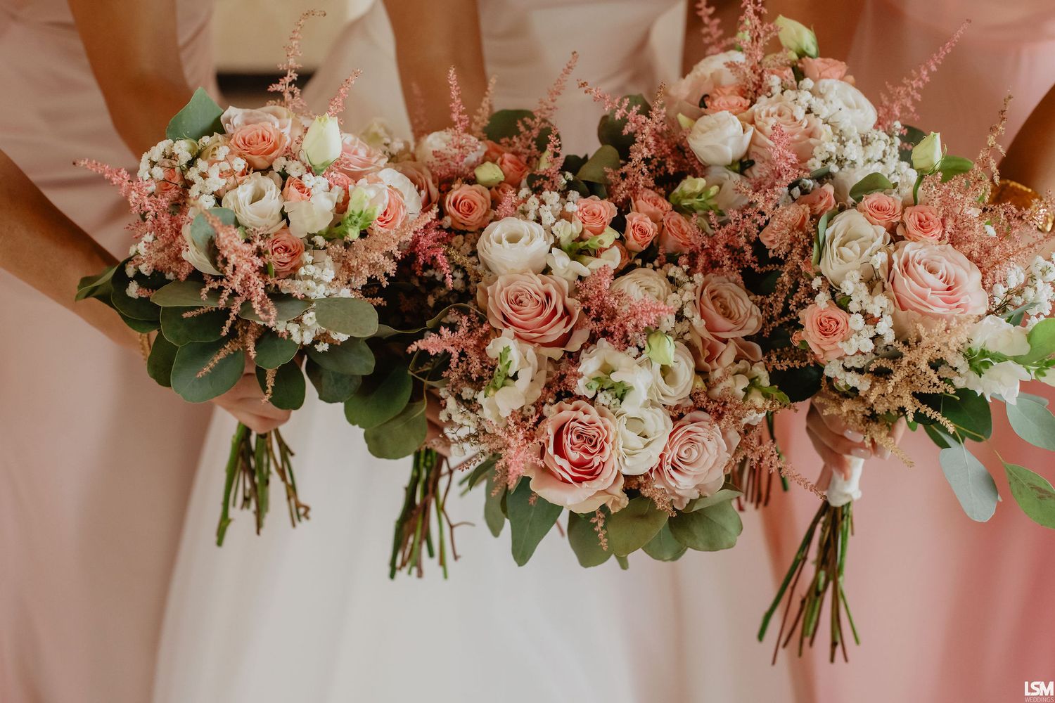 Bridesmaids holding lush pink and white wedding bouquets with roses and eucalyptus at a wedding ceremony.