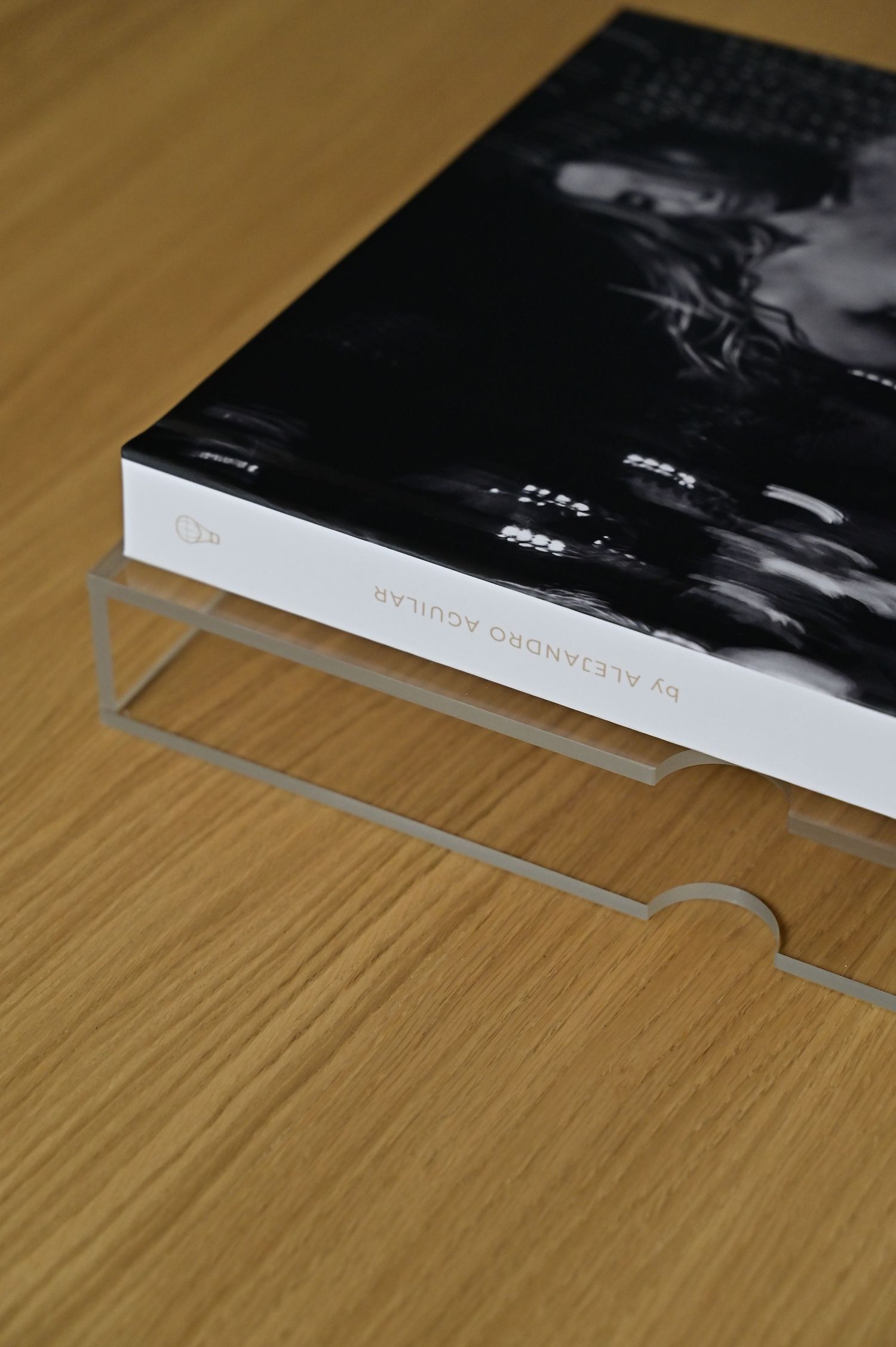Photography book by Alejandro Aguilar displayed on a clear acrylic stand on a wooden table.