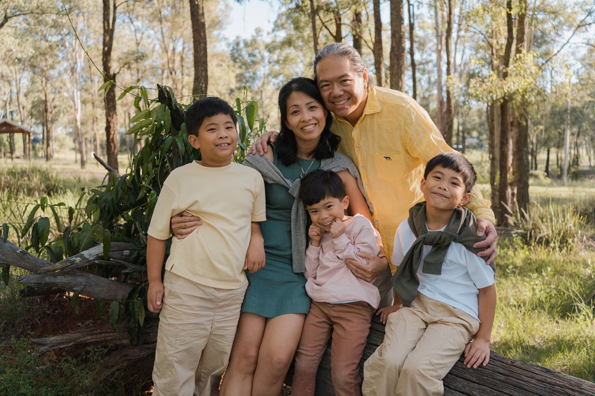 Happy Asian family of five posing outdoors in a sunny forest park, smiling together for a family photo session in rouse hill regional park