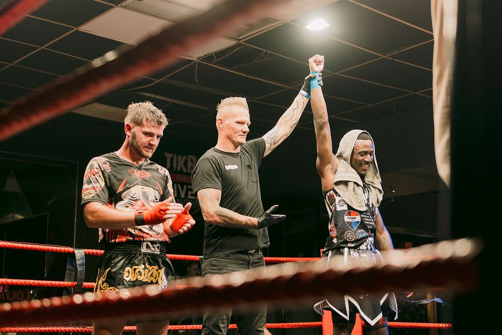 A referee raises a fighter's hand in victory inside a boxing ring after a Muay Thai match.