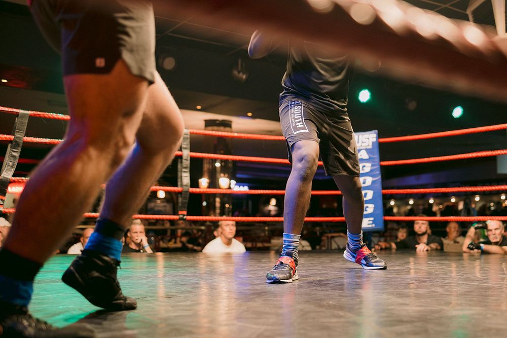 Two boxers sparring in a professional boxing ring under dim lights during a live match event.
