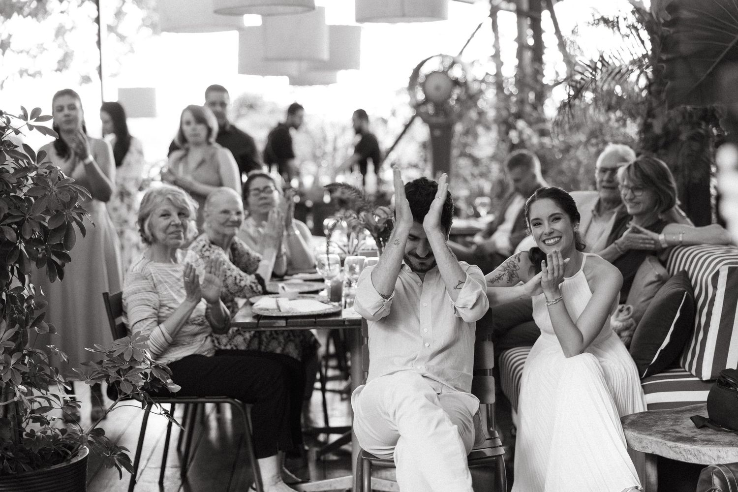 Black and white candid photo of joyful wedding guests laughing and celebrating at an outdoor reception.