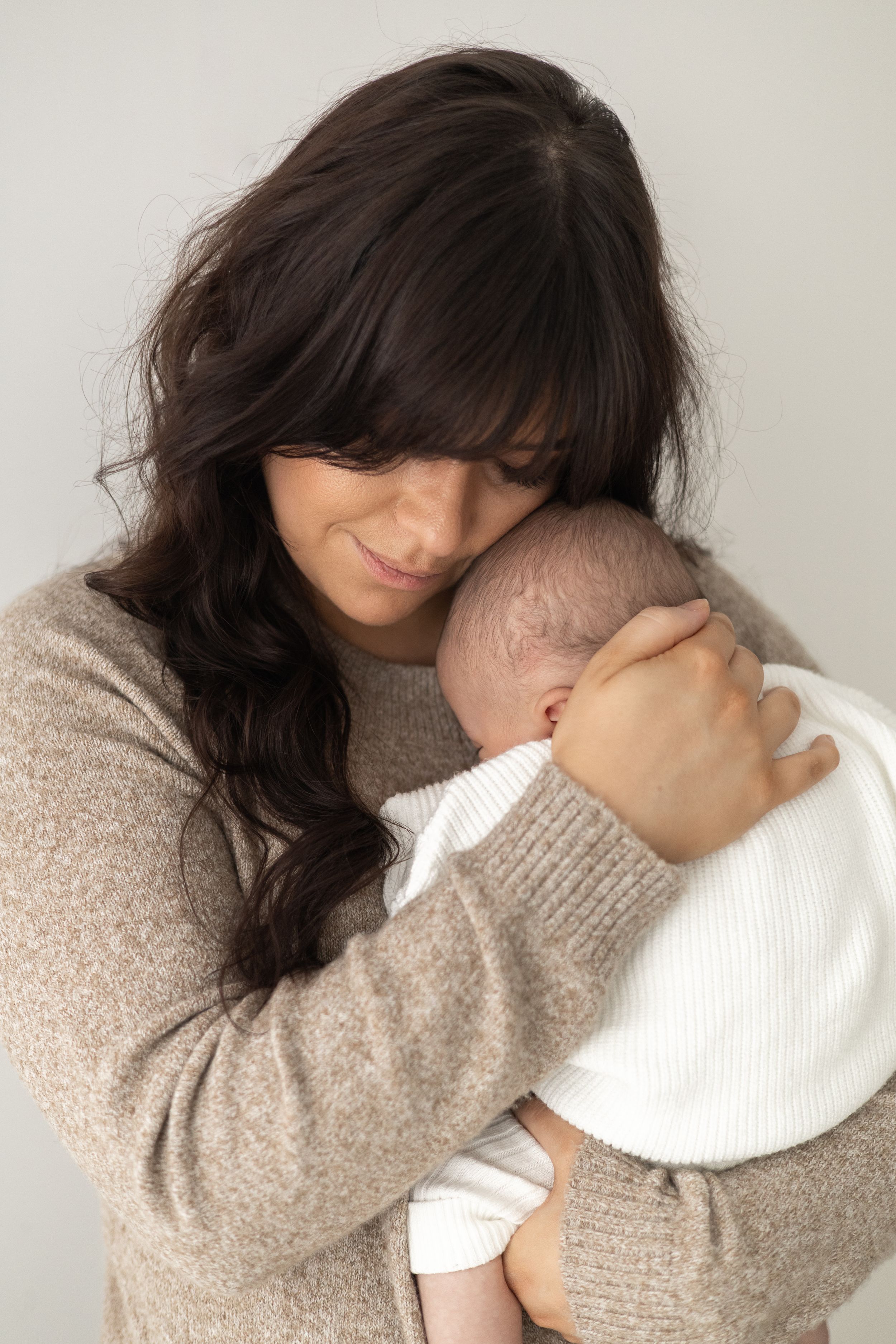 Mum in a beige jumper tenderly holds a newborn baby against her shoulder natural older newborn baby photography Nottingham