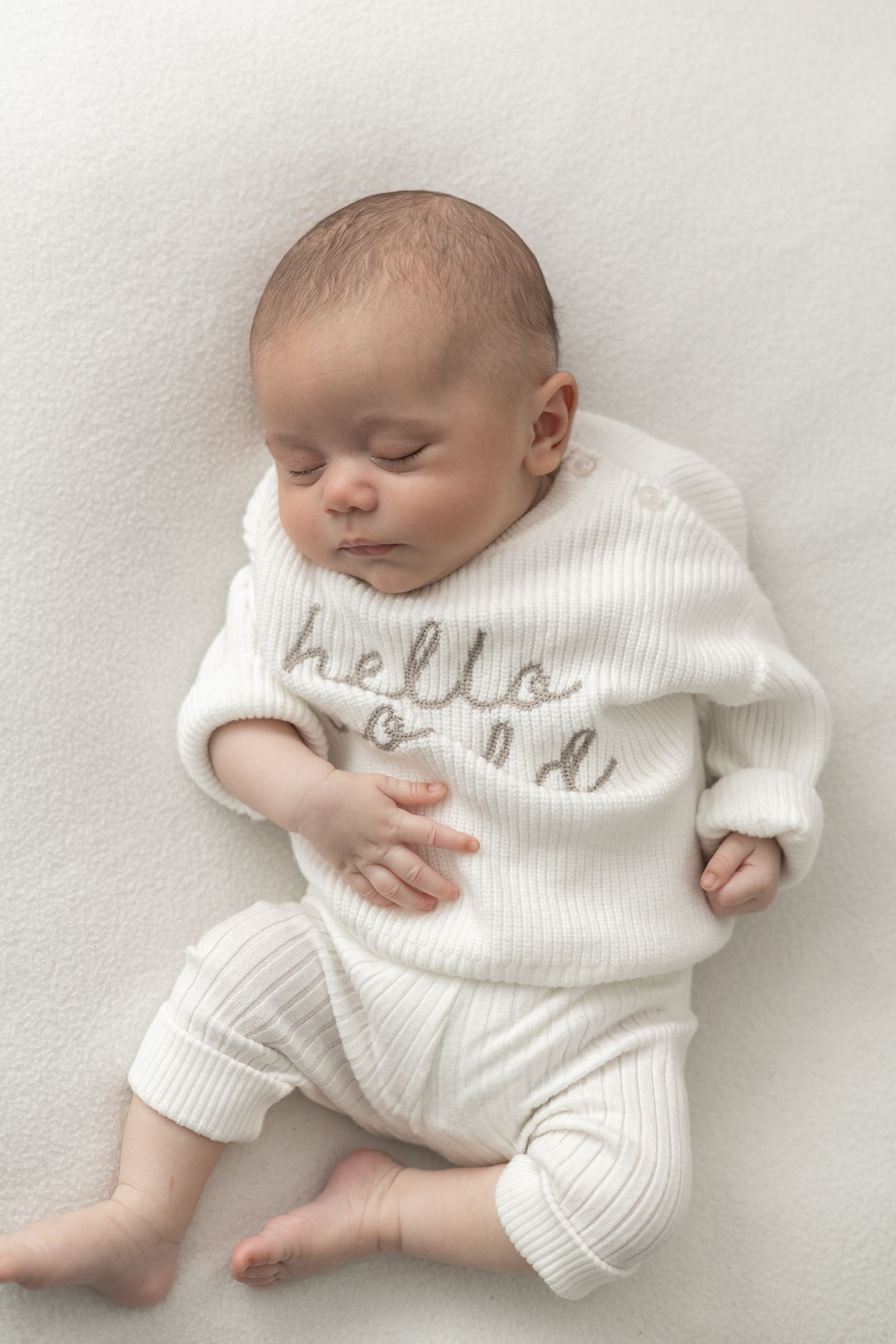 Sleeping newborn baby in white ribbed hello world outfit lying on soft white blanket natural older newborn baby photography Nottingham