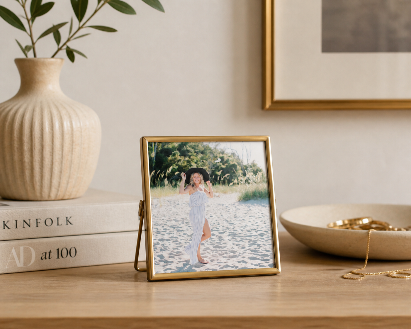 Gold brass photo frame on wooden shelf with ceramic vase, books, and decorative neutral home decor setting of a senior posing in Hilton Head