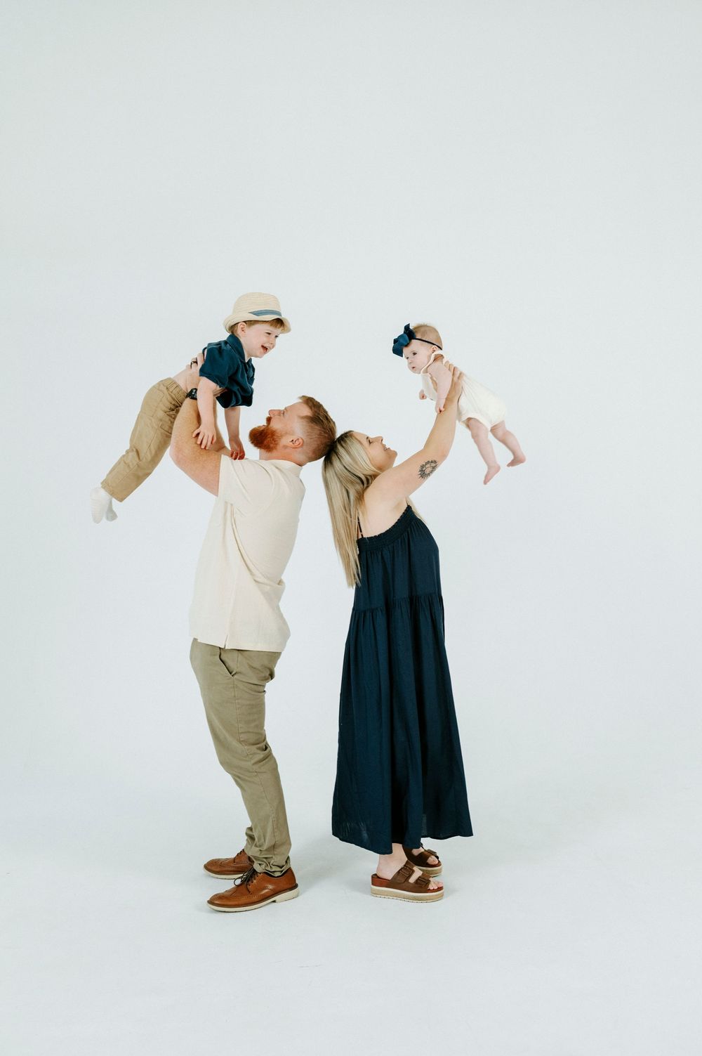Happy family with two parents lifting their young children in a bright white studio photo session.