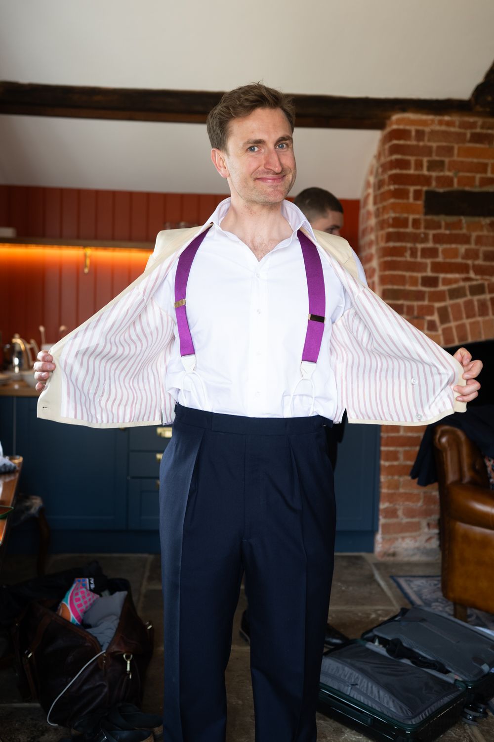 Man in white shirt with purple suspenders proudly showing off his outfit while getting ready for a formal event.