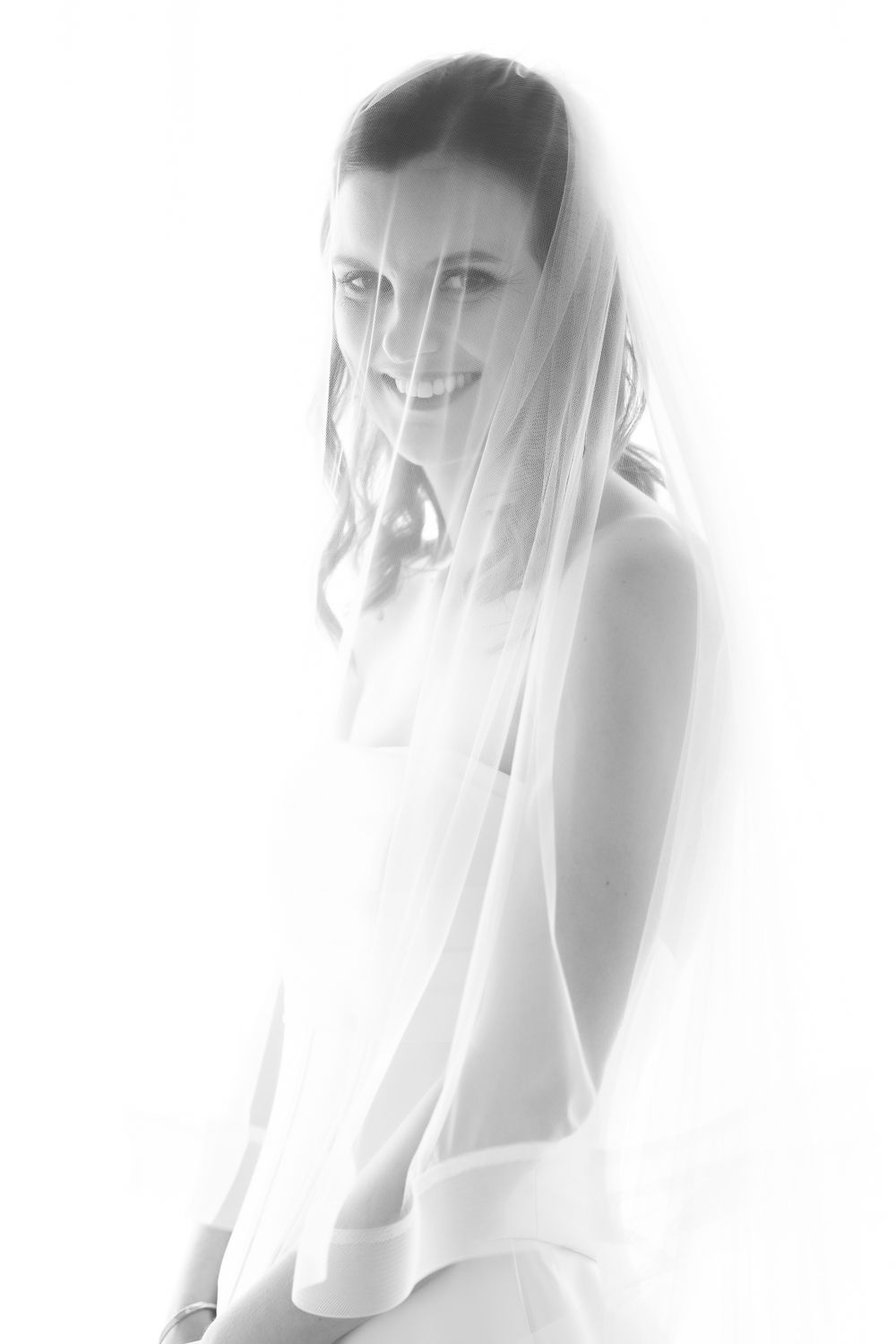 Smiling bride in white dress and veil, elegant black and white wedding portrait photography.