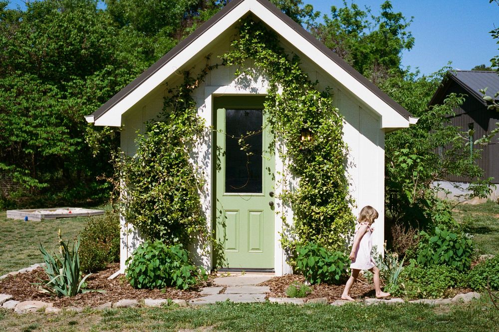 Charming white cottage with green door covered in climbing vines, with a young child standing in the garden.