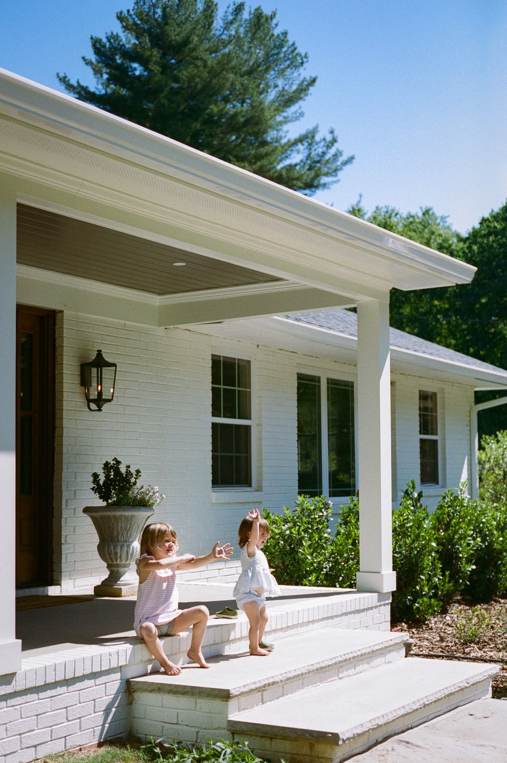 Two young children playing on the front porch steps of a white brick house.