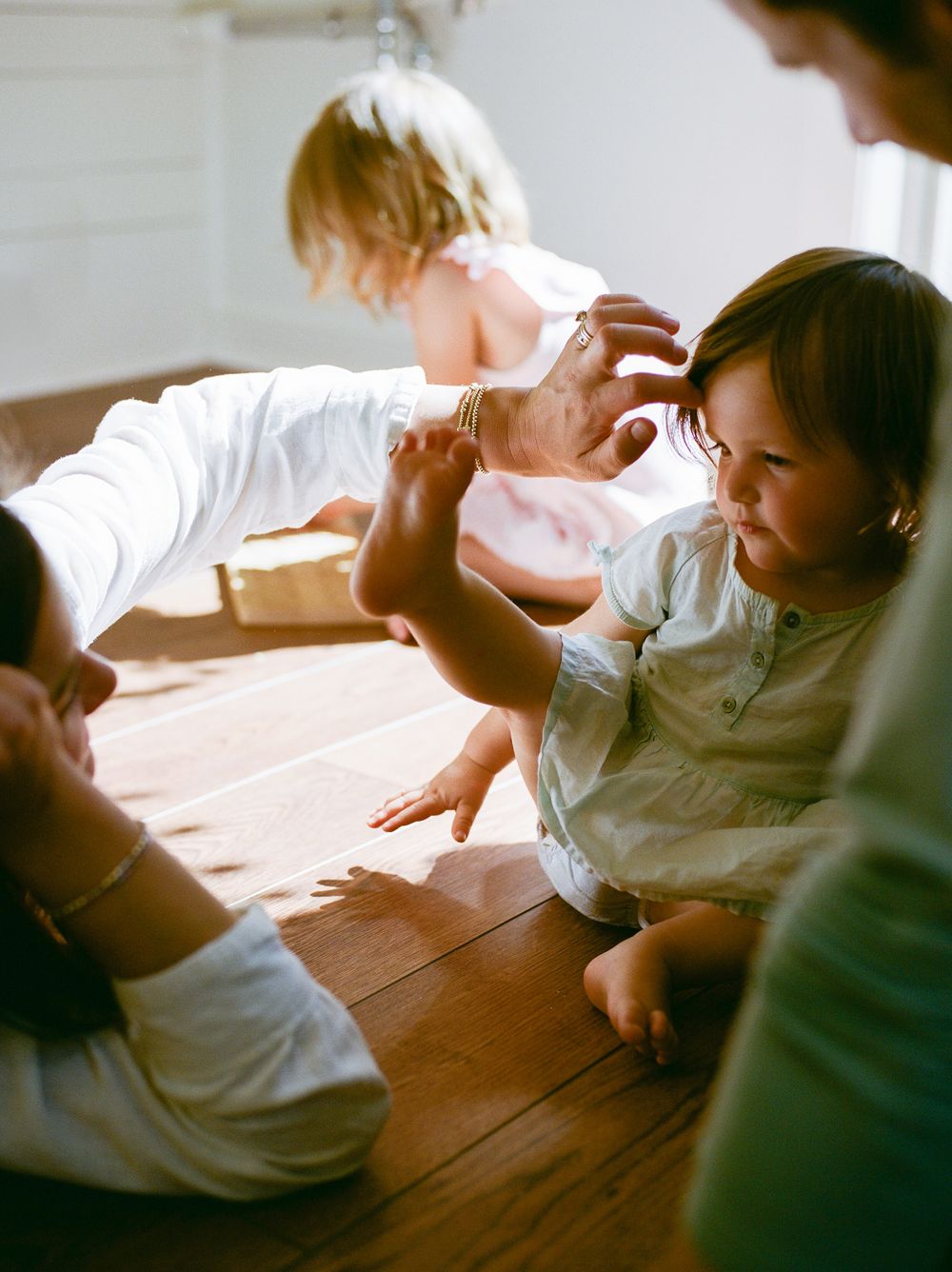 Young children playing together on a hardwood floor indoors in soft natural light.