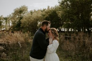 Romantic couple sharing a tender moment surrounded by tall grasses and trees.