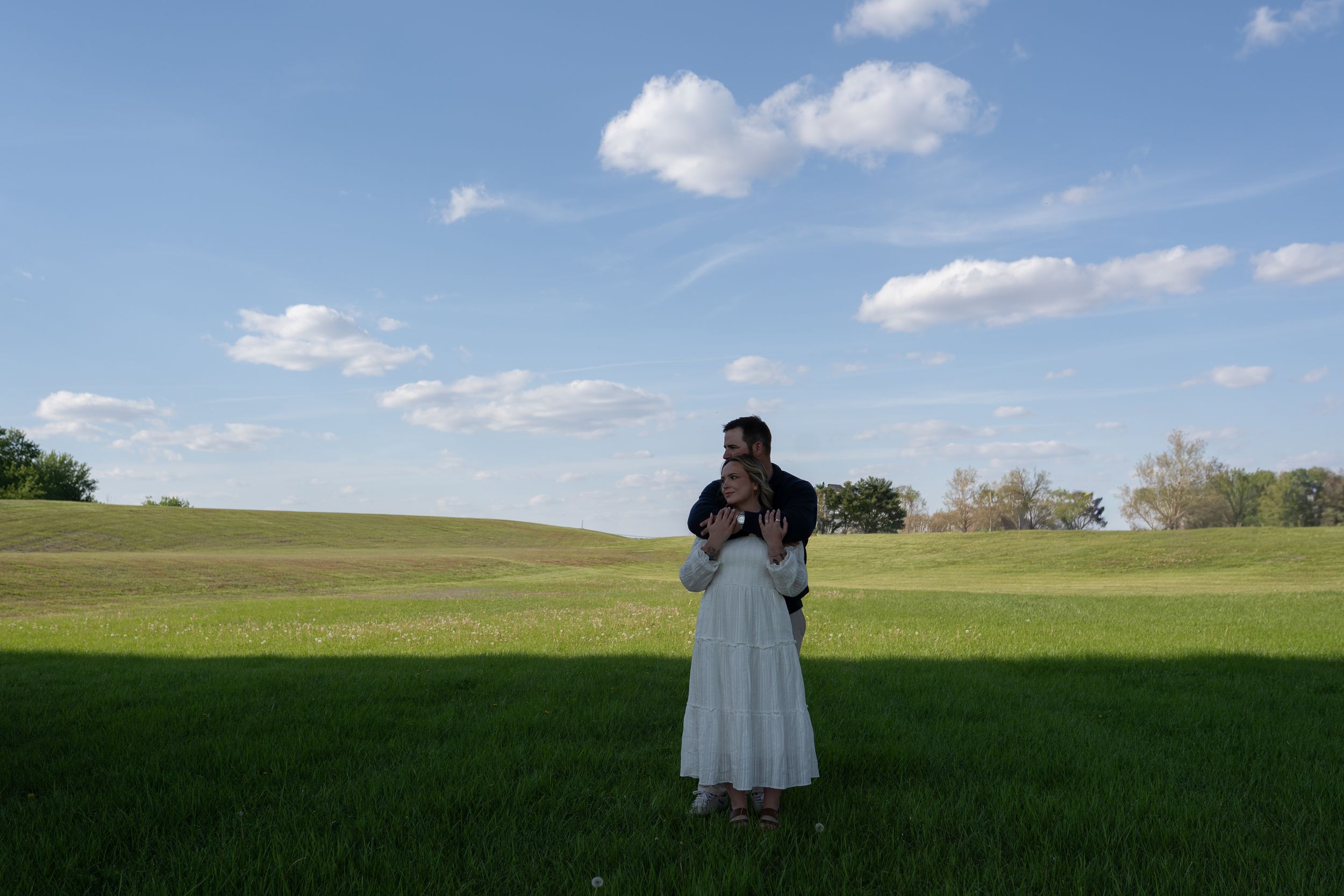 Woman in white dress standing in a green field under a blue sky with clouds.