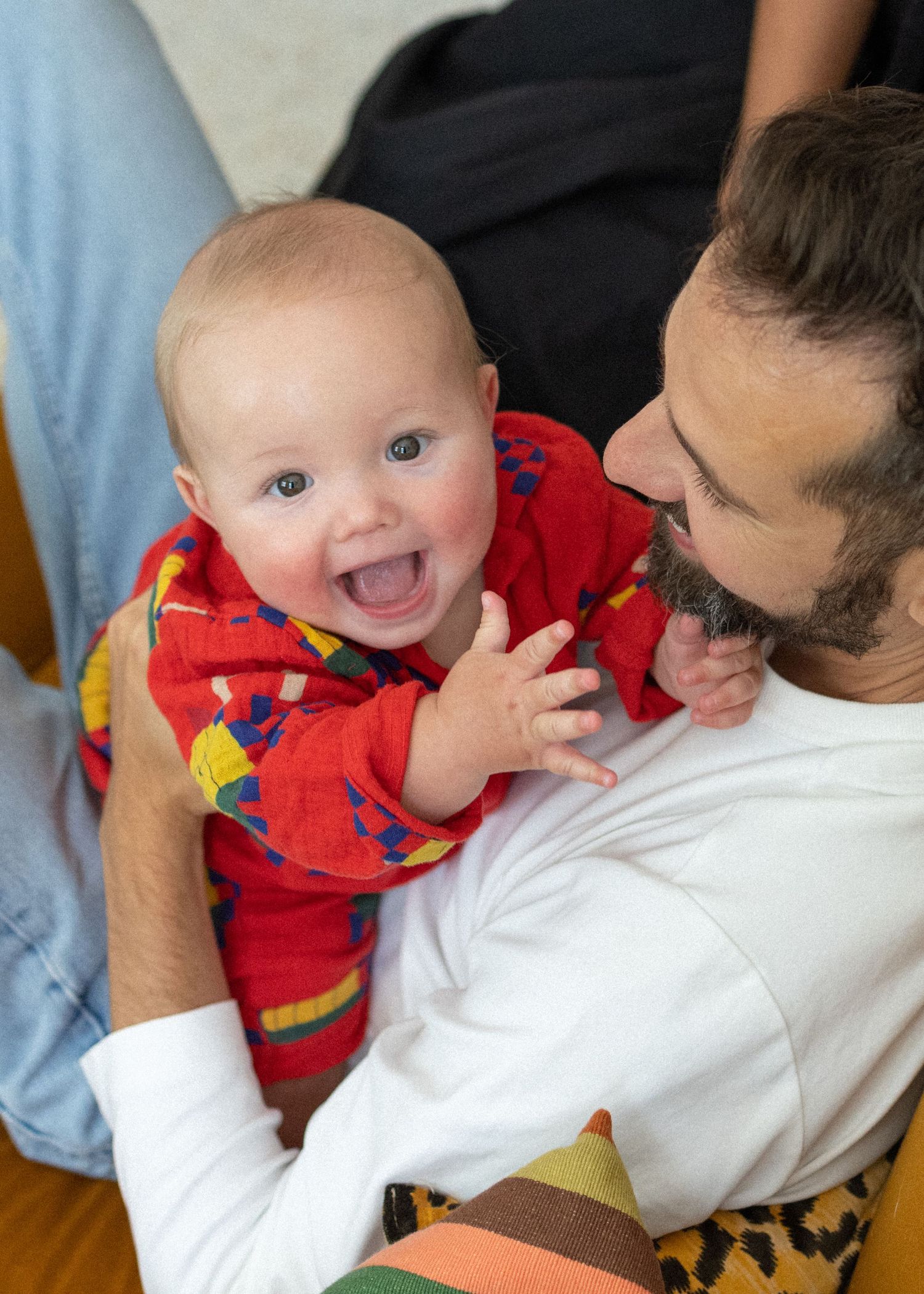 Happy young parents smiling at their newborn baby in a sunny outdoor setting, mother wearing brown off-shoulder top.