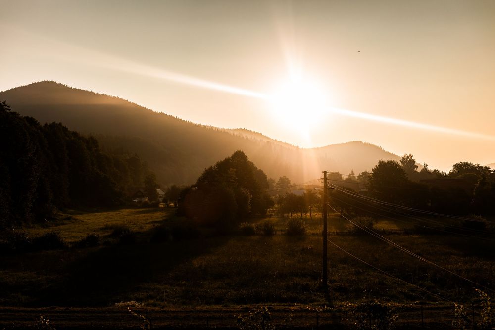 Golden sunset casting warm light over a scenic mountain valley with trees and rolling hills.