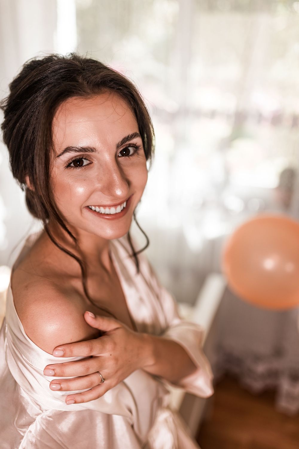 Smiling brunette woman in a satin robe hugging herself, with a peach balloon in the background.