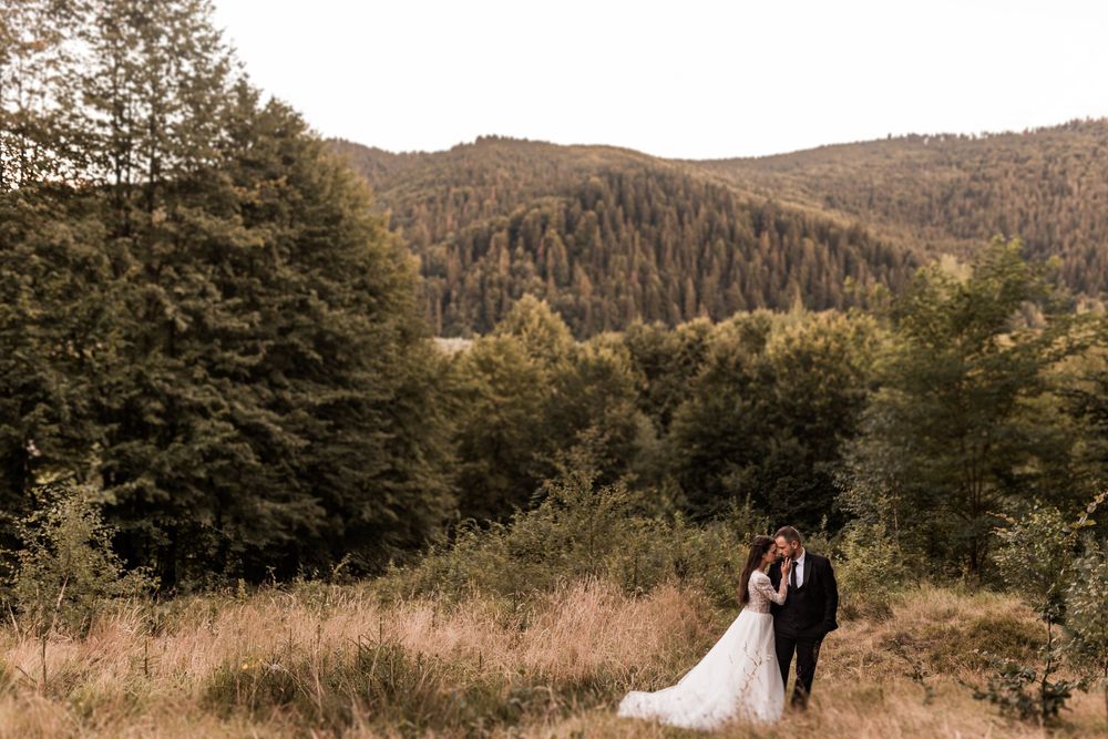 Wedding couple embracing in mountain meadow surrounded by autumn forest landscape.