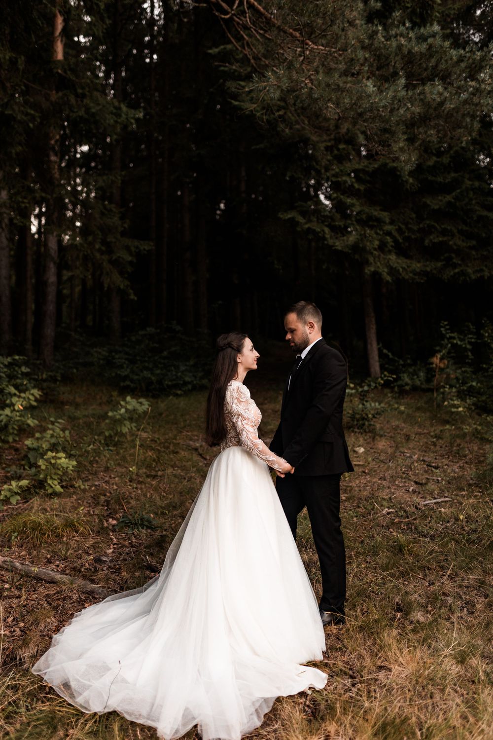 Bride and groom holding hands in romantic forest setting during wedding photoshoot.