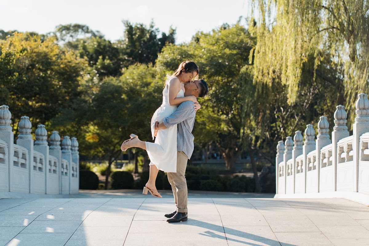 Couple sharing a romantic embrace on a sunlit bridge surrounded by lush green trees in western sydney nurrugingy park photoshoot