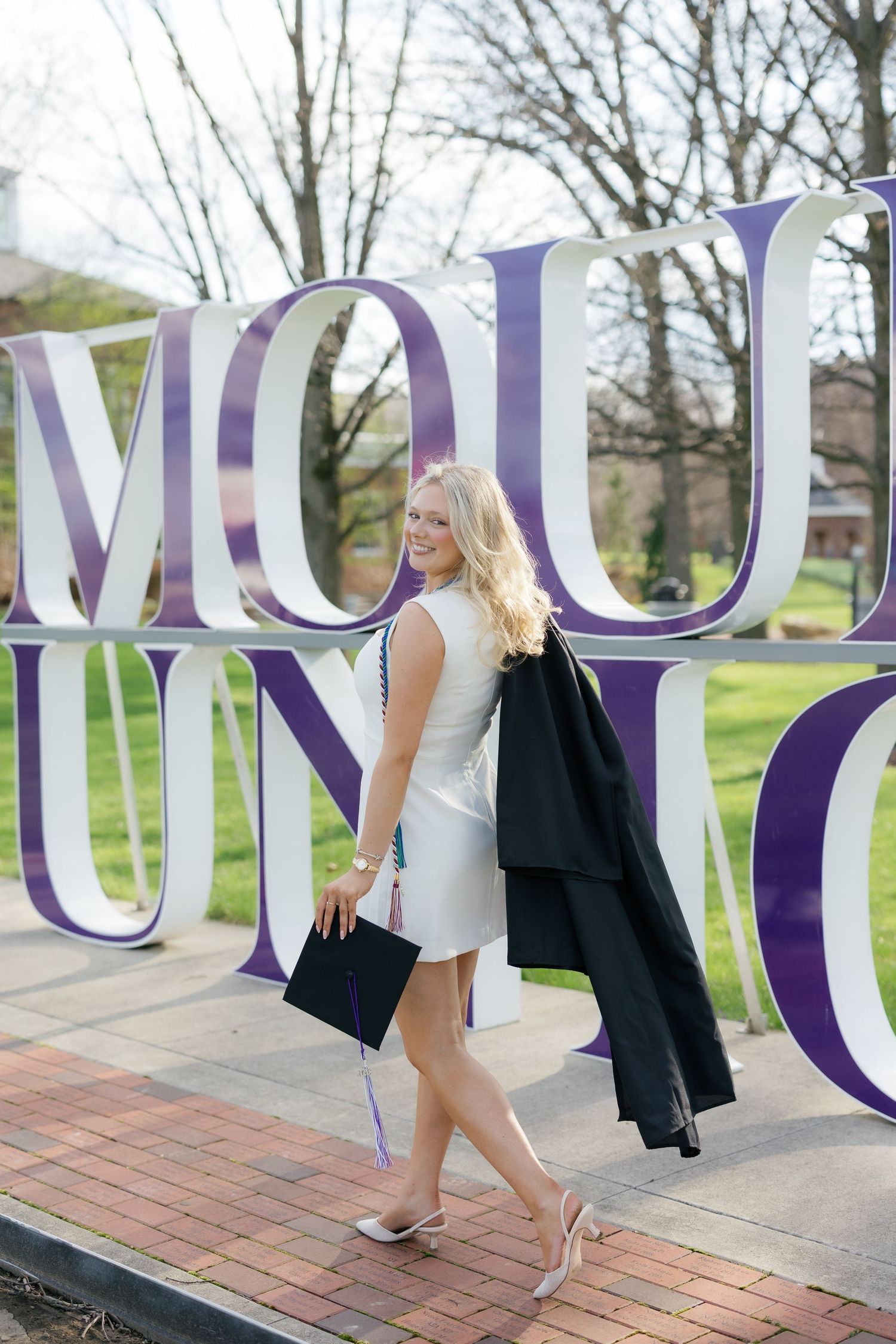 Smiling blonde graduate posing with cap and gown beside large Mount Union university sign.