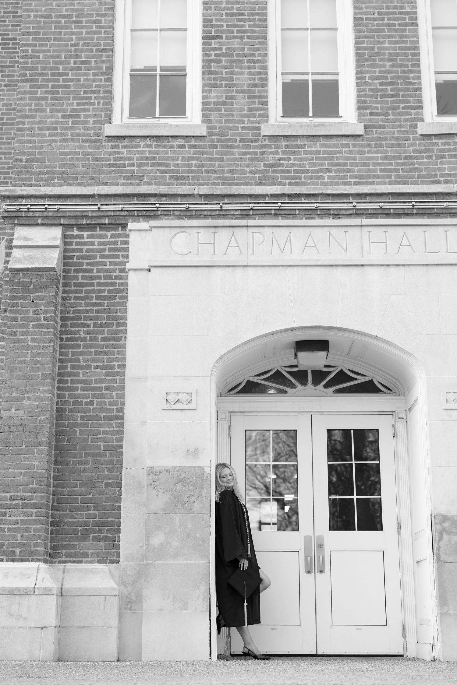 Blonde woman in black outfit poses at entrance of Chapman Hall in black and white photo.