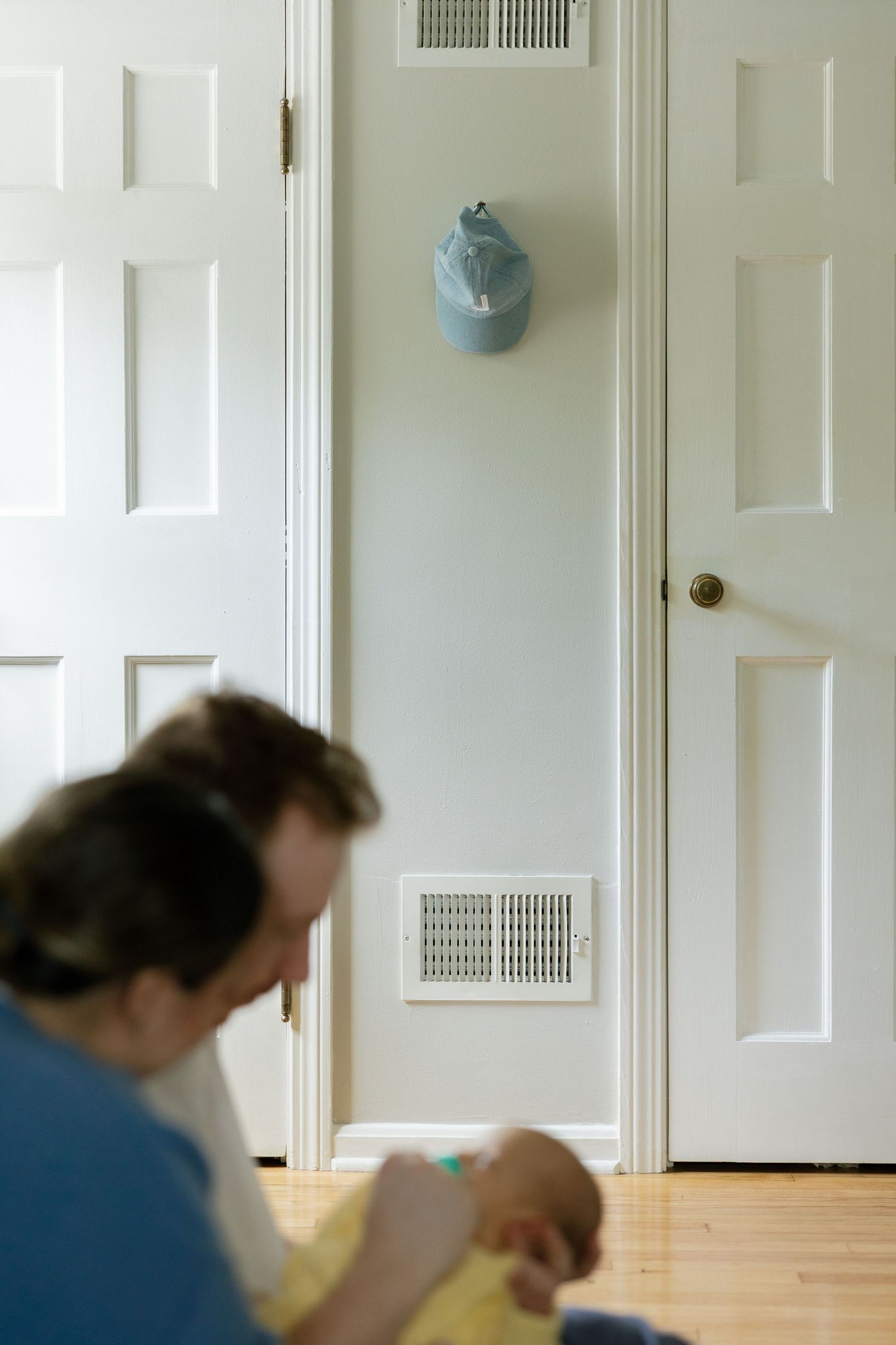 A father tenderly holds his newborn baby on the floor of a cozy nursery room with white doors and hardwood floors.
