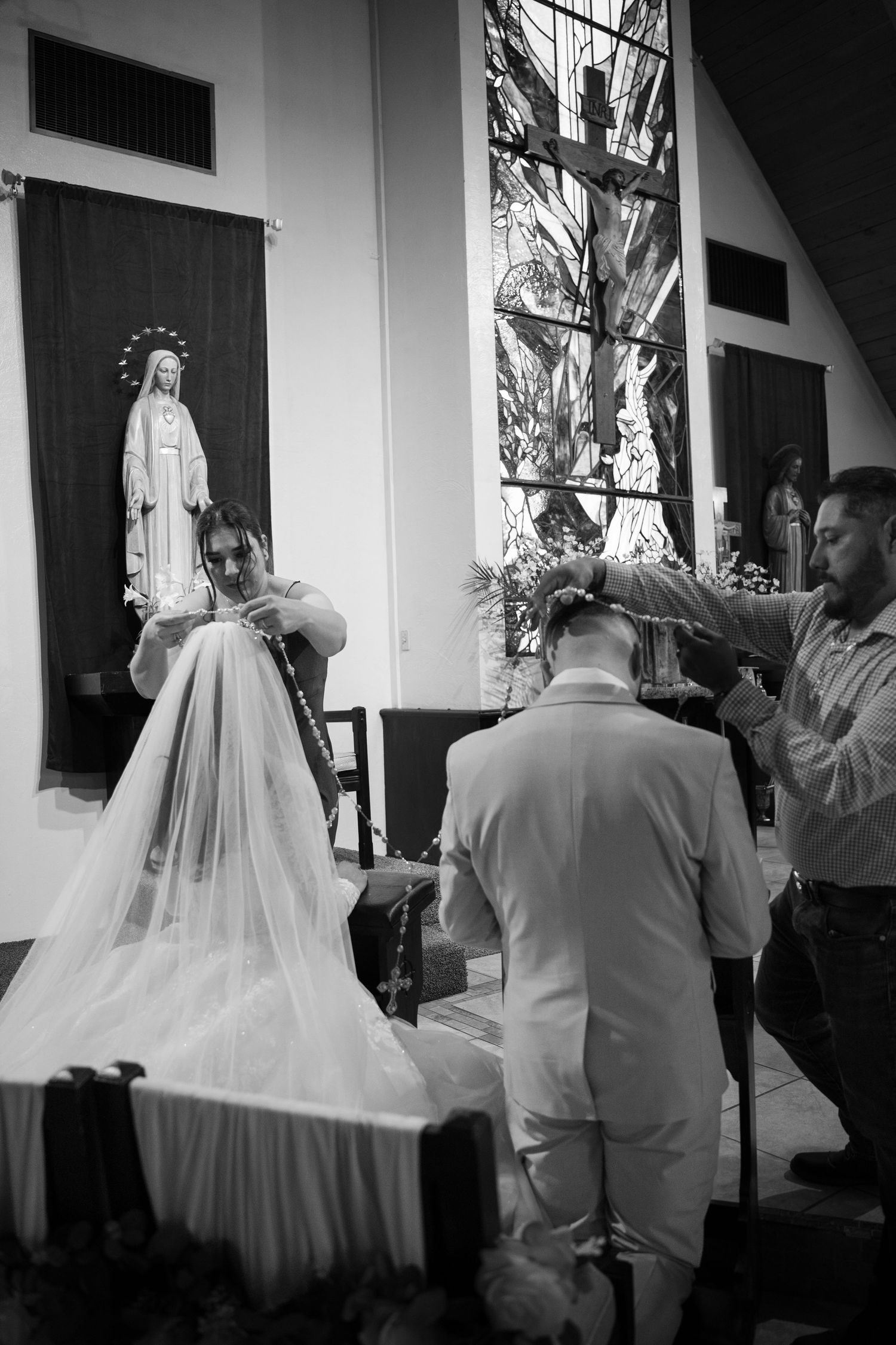 Black and white photo of a bride and groom kneeling at church altar during Catholic wedding ceremony.