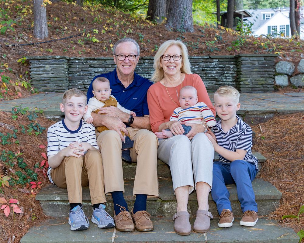 Family portrait of grandparents sitting on stone steps with four young grandchildren in autumn during a family photo session in Sudbury, MA.