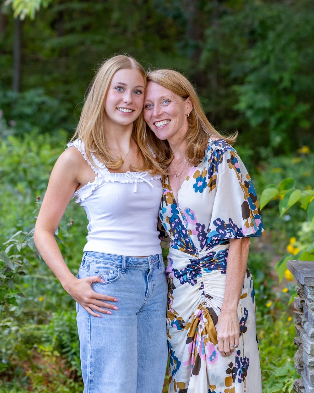 High school senior daughter & mom pose together outdoors in a lush green garden during a family photo session in Sudbury, MA.