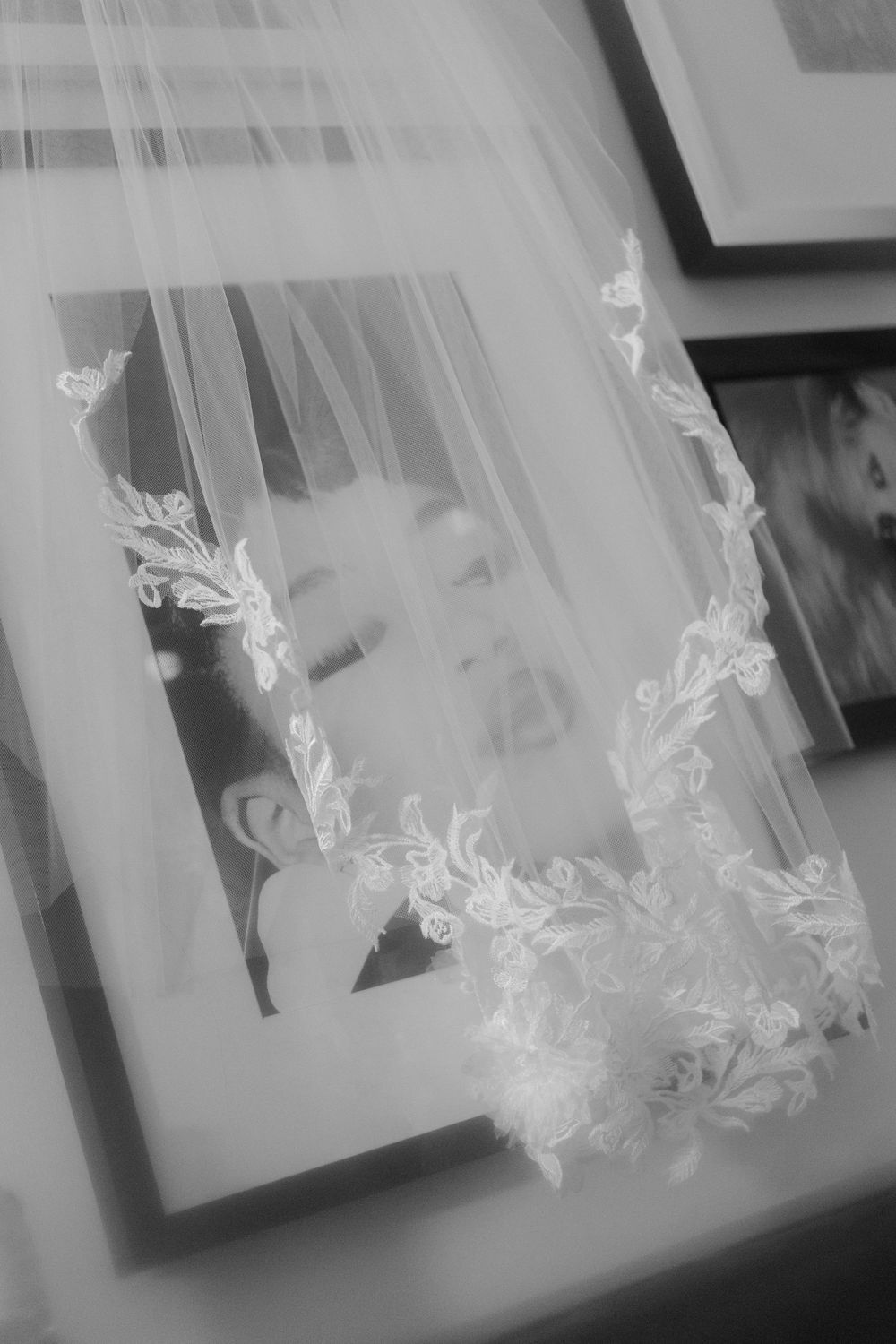A delicate white bridal veil with floral lace embroidery lies elegantly draped near a photo frame in black and white.