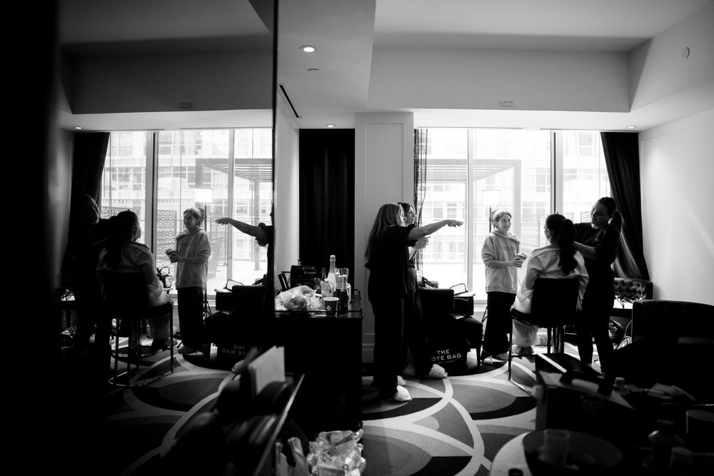 Black and white silhouette photo of people getting ready in a bright hotel room with large windows.