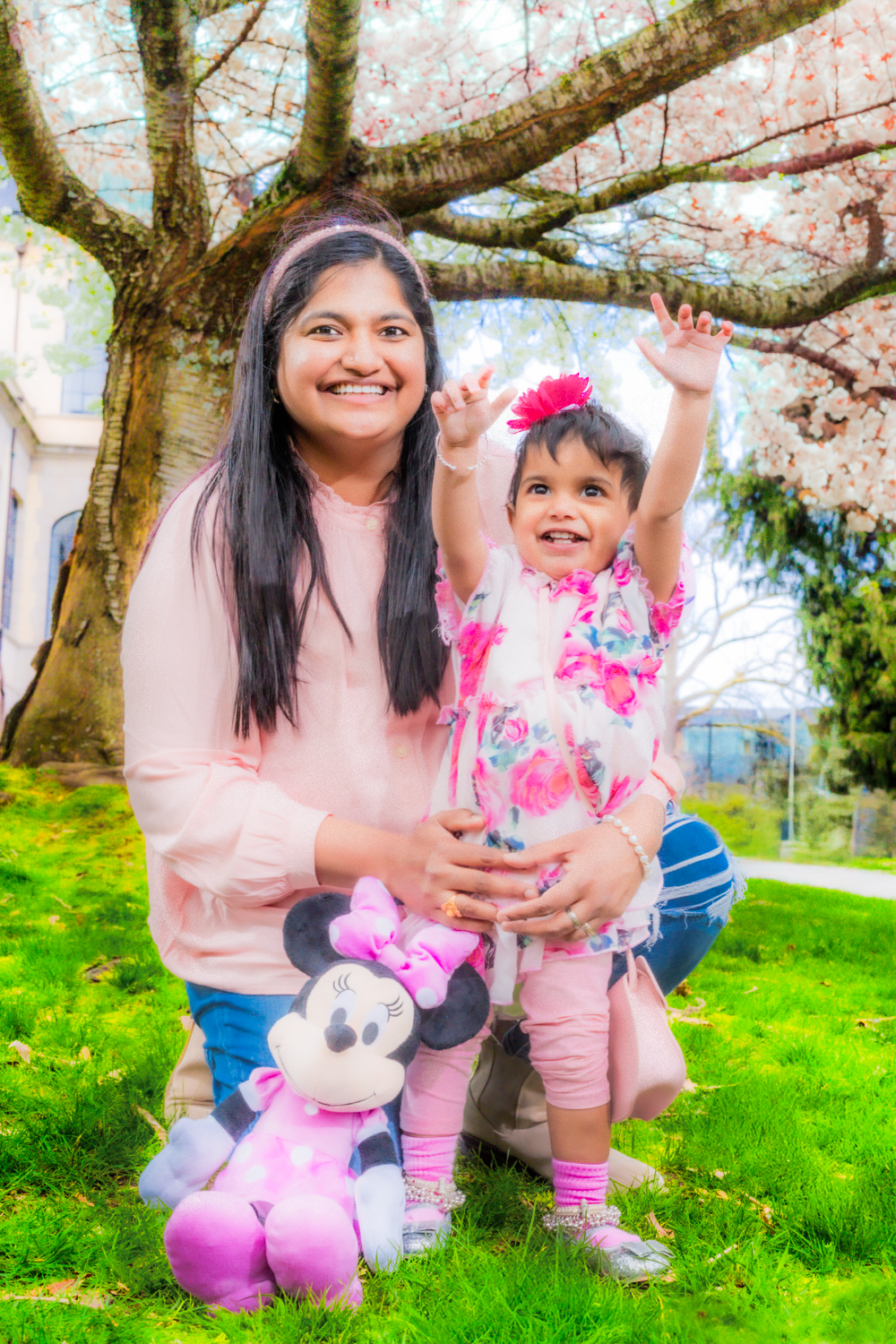 Springtime portrait under a cherry blossom tree with a Minnie Mouse plush toy on green grass.